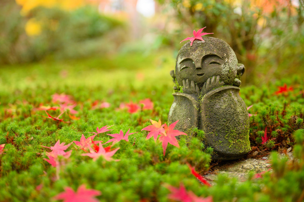 Rotes Ahornblatt auf einer kleinen buddhistischen Mönchsstatue (Jizo) im japanischen Garten