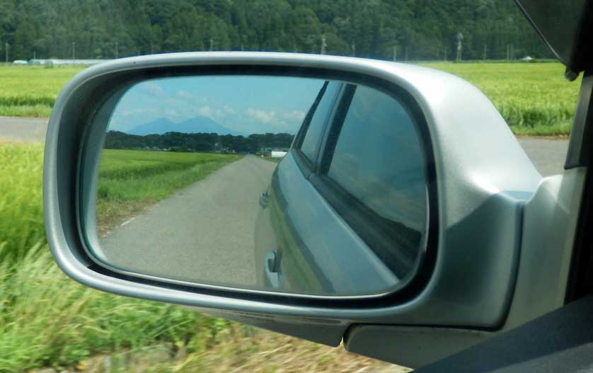 Mount Bandai seen in the rearview mirror of a car.