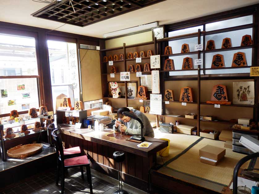 Shogi piece craftsman at work inside the Eishundo Shogi Store, Tendo.