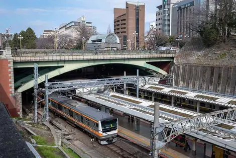 Yotsuya-mitsume Bridge (part of Shinjuku-dori Avenue) over Yotsuya Station, with Kojimachi Exit on far side of road Yotsuya-mitsume Bridge (part of Shinjuku-dori Avenue) over Yotsuya Station, with Kojimachi Exit on far side of road