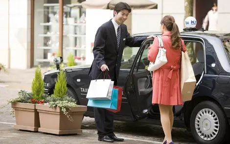 A porter opening the door of a Japanese taxi to a client.