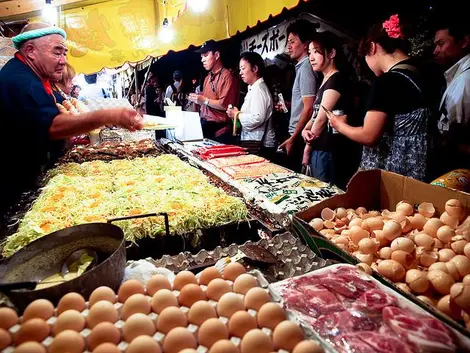 Visitantes comprando okonomiyaki o yakisoba en un puesto de comida.