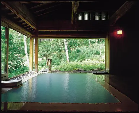 Onsen entre intérieur et extérieur, entouré par une nature luxuriante