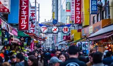 Crowds of people in a street, lined with shops, shop and cafe signs. 