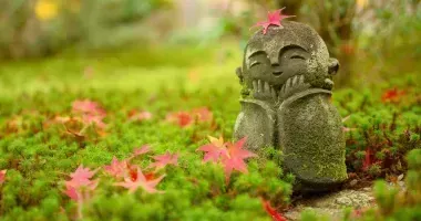 Foglia di acero rossa sulla testa della piccola roccia della bambola del monaco buddista nel giardino giapponese