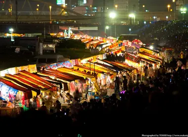 En las orillas del río Yodogawa, las multitudes luchan por obtener los mejores puestos para ver los fuegos artificiales. En las orillas del río Yodogawa, las multitudes luchan por obtener los mejores puestos para ver los fuegos artificiales.