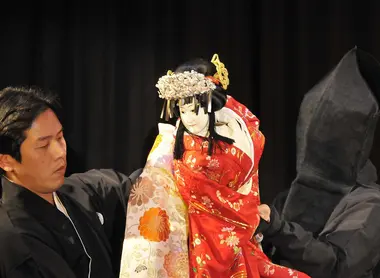 Un marionnettiste a visage découvert, manipulant sa marionnette.