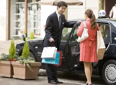 A porter opening the door of a Japanese taxi to a client.