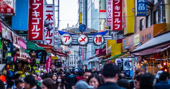 Crowds of people in a street, lined with shops, shop and cafe signs. 