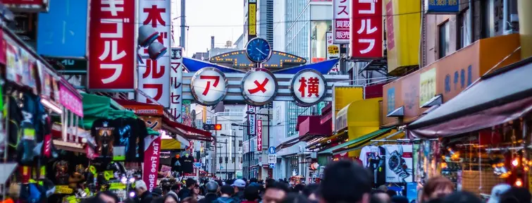 Crowds of people in a street, lined with shops, shop and cafe signs. 