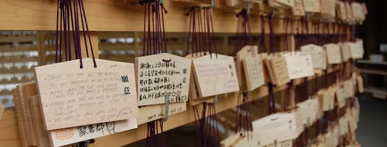 Small wooden plaques with wishes written in Japanese hanging on a stand